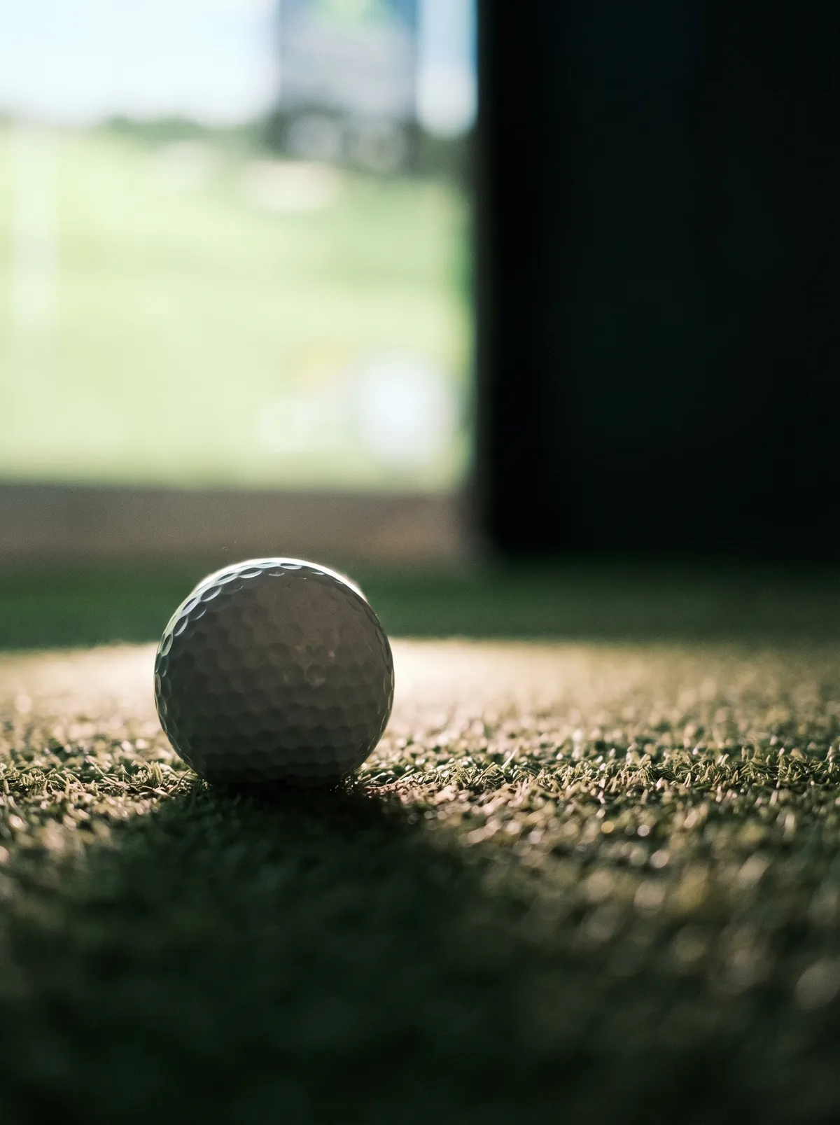 Low angle view of a golf ball on simulator turf with impact screen in background