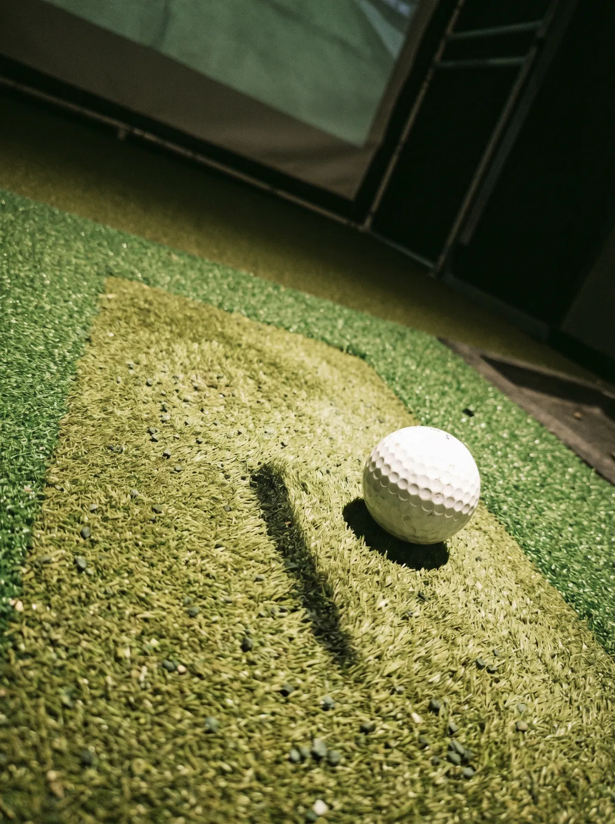 Golf ball on a commercial hitting mat inside a simulator bay